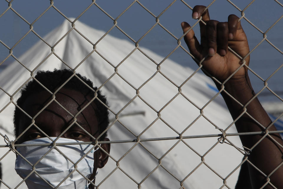 Emanuel Conteh migrant from Sierra Leone wearing a face mask stands behind a fence inside a refugee camp in Kokkinotrimithia outside of capital Nicosia, Cyprus, Friday, Feb. 5, 2021. Cyprus' Interior Minister Nicos Nouris said this week that the east Mediterranean island nation whose closest point to Syria is around 150 kilometers (93 miles) remains first among all other European Union member states with the most asylum applications relative to its population. Last year, the country of around 1.1 million people racked up 7,000 asylum applications - most of them from Syrians. (AP Photo/Petros Karadjias)