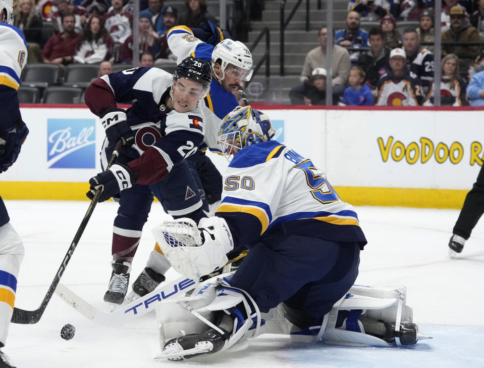 Colorado Avalanche center Ross Colton, left, tries to redirect the puck at St. Louis Blues goaltender Jordan Binnington after driving past defenseman Justin Faulk during the third period of an NHL hockey game Saturday, Nov. 11, 2023, in Denver. (AP Photo/David Zalubowski)