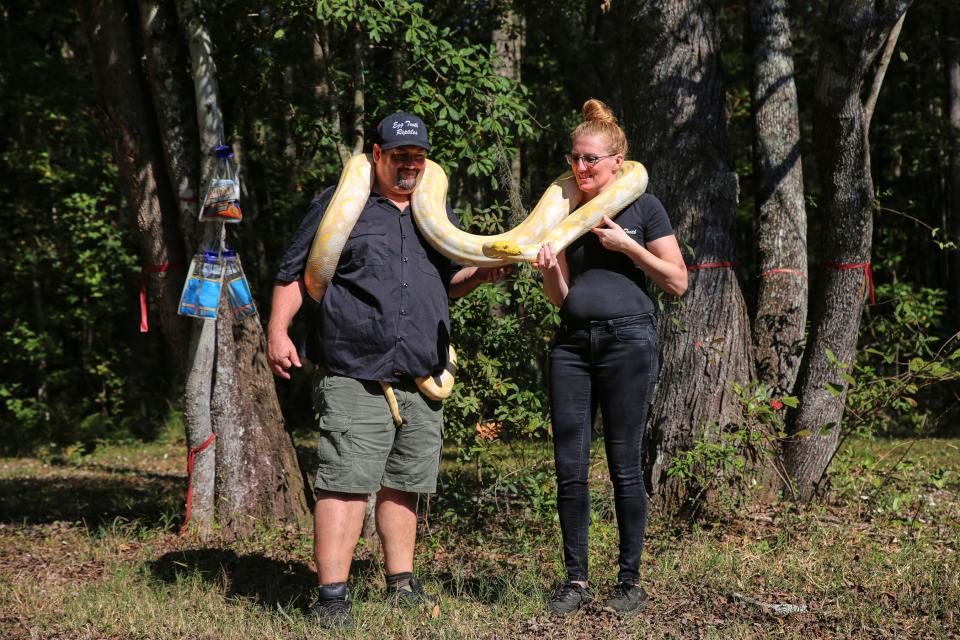 John McHugh (left) and Michelle Watts (right) holding up one of their larger pythons in their backyard on Wednesday, November 2, 2022.