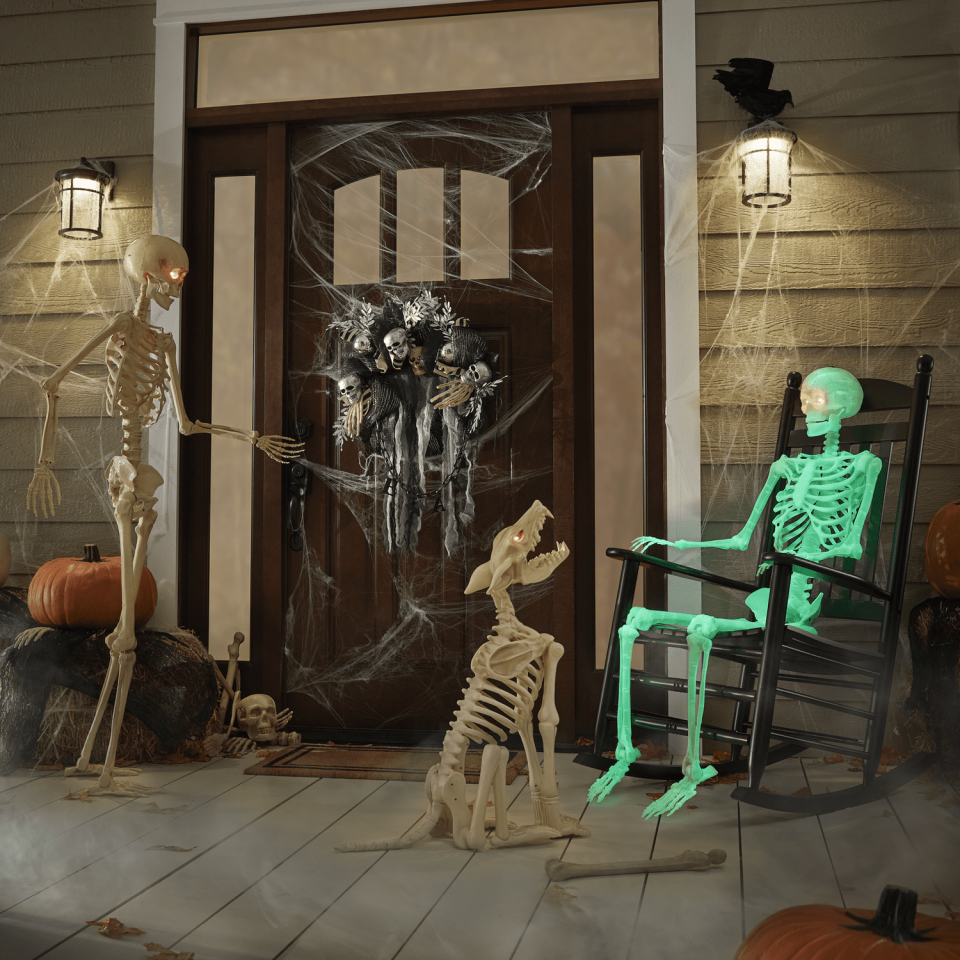 Dark front porch with a green skeleton in a rocking chair next to a plastic wolf skeleton