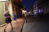 FILE - In this March 23, 2020 file photo, Jessica Fender, center, and Kerry Maloney, left, shy away from a woman asking for money after they felt she got too close, as the two exercise social distancing due to the new coronavirus outbreak, on a deserted Bourbon Street in New Orleans. Where political divides marred early recovery efforts after Hurricane Katrina in 2005, Louisiana is showing rare political unity in the fight against the new coronavirus. (AP Photo/Gerald Herbert, File)