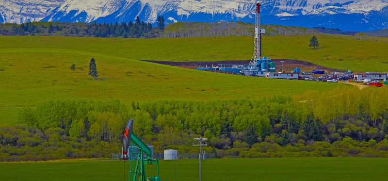 A drilling rig and pump jack with mountains in background.