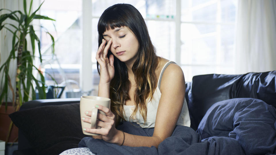 Woman sat up, rubbing her eyes and looking tired, with a mug in her hand