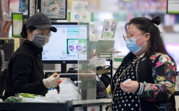 A grocery store worker wears a protective face mask and gloves as a customer stands on the other side of a plexiglass divider in downtown Vancouver Wednesday, April 29, 2020.