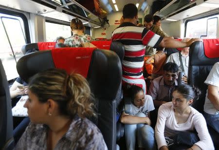 Travellers sit in a train with migrants on board, en route from Budapest to Vienna, Austria, August 31, 2015. REUTERS/Laszlo Balogh