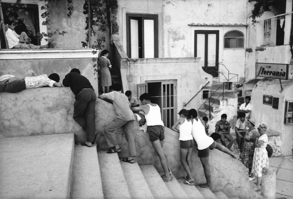 Ni&#xf1;os y j&#xf3;venes italianos en los escalones de un callej&#xf3;n. A la derecha se observa un cartel publicitario de las pel&#xed;culas fotogr&#xe1;ficas Ferrania en Capri, 1960 (Fotograf&#xed;a de Mario De Biasi;Walter Mori;Emilio Ronchini/Mondadori v&#xed;a Getty Images)