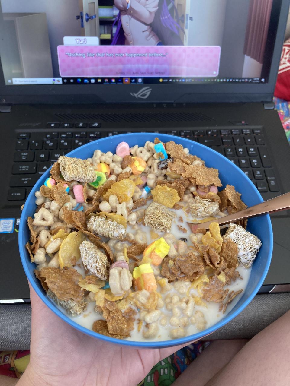 A person holding a bowl of cereal in front of a laptop screen