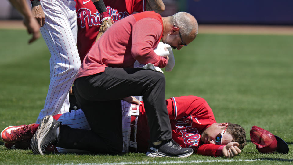 A trainer checks on Philadelphia Phillies first baseman Rhys Hoskins after he was injured fielding a ground ball by Detroit Tigers' Austin Meadows during the second inning of a spring training baseball game Thursday, March 23, 2023, in Clearwater, Fla. Hoskins had to be carted off the field. (AP Photo/Chris O'Meara)