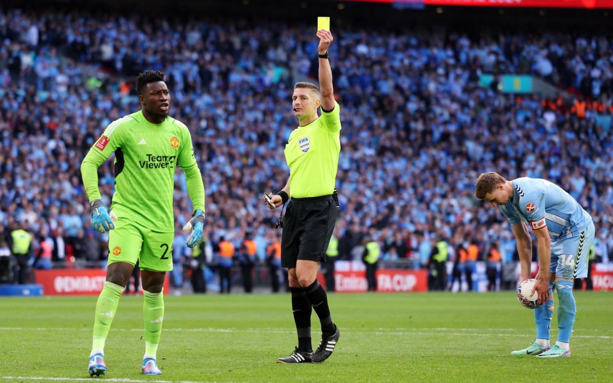 Referee Robert Jones shows a yellow card to Andre Onana