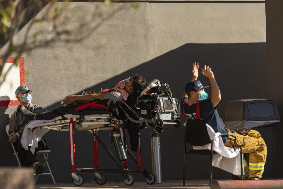 An unidentified patient receives oxygen on a stretcher, while Los Angeles Fire Department Paramedics monitor him outside the Emergency entrance, waiting for a room at the CHA Hollywood Presbyterian Medical Center in Los Angeles Friday, Dec. 18, 2020. Increasingly desperate California hospitals are being "crushed" by soaring coronavirus infections, with one Los Angeles emergency doctor predicting that rationing of care is imminent. (AP Photo/Damian Dovarganes)