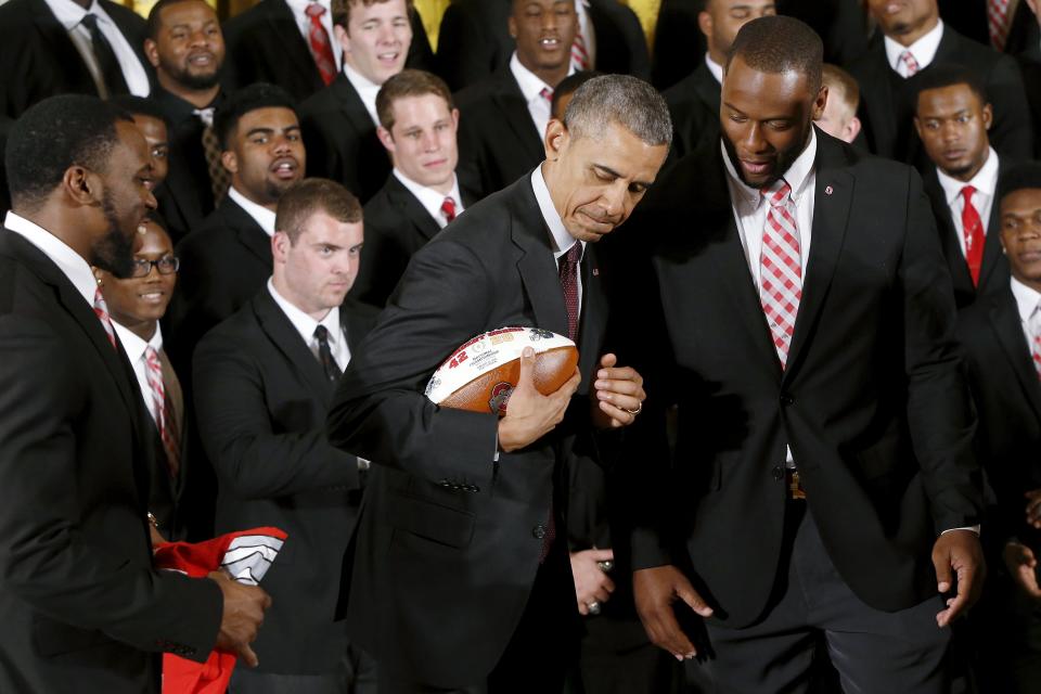 U.S. President Barack Obama plays with a football he received from Ohio State team captains Doran Grant (L) and Curtis Grant (R) as he plays host to the reigning NCAA football champion Buckeyes in a reception in the East Room of the White House in Washington, April 20, 2015. REUTERS/Jonathan Ernst