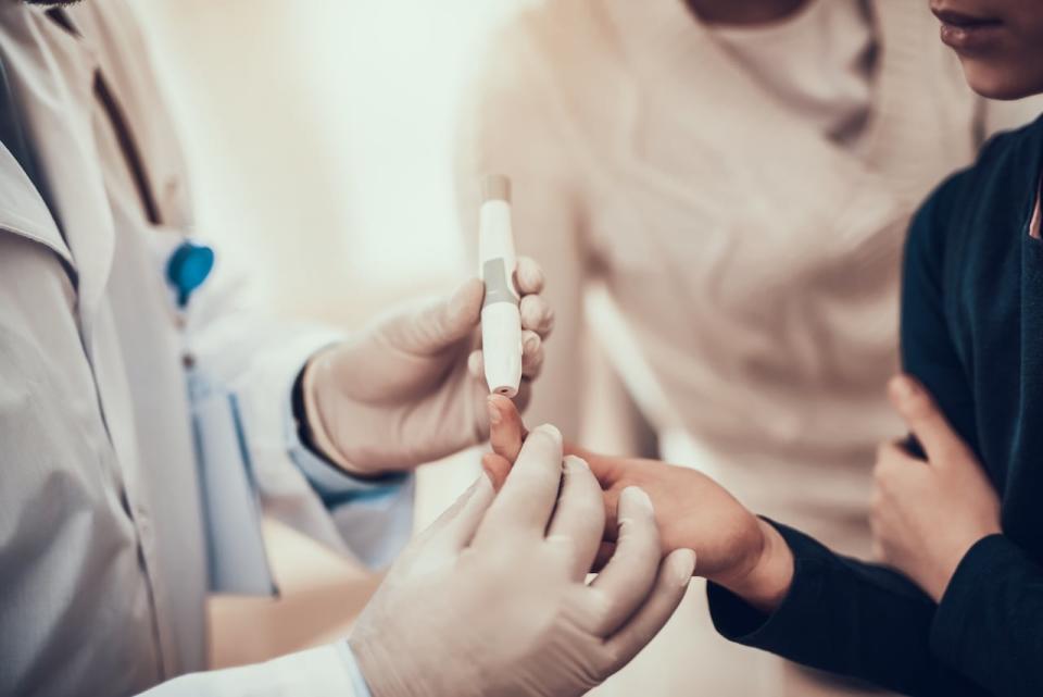 An Indian doctor wearing a white gown is examining a patient in his office. Doctors use glucometers to measure blood sugar levels. Photo ID: 1294037032