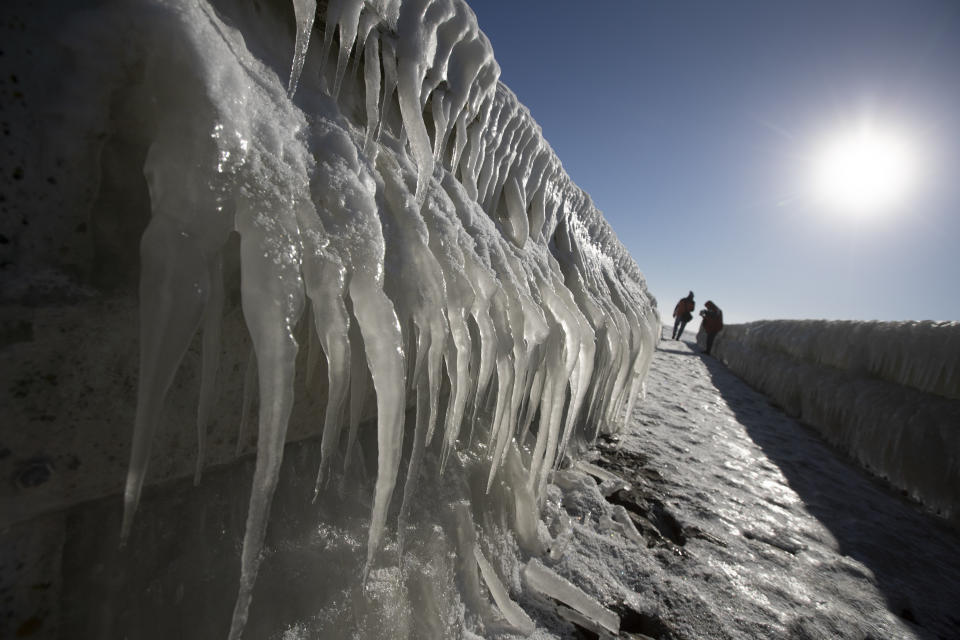 People take pictures of icicles on a jetty at the Afsluitdijk, a dike separating IJsselmeer inland sea, rear, and the Wadden Sea, Netherlands, Thursday, Feb. 11, 2021. The deep freeze gripping parts of Europe served up fun and frustration with heavy snow cutting power to some 37,000 homes in central Slovakia. (AP Photo/Peter Dejong)