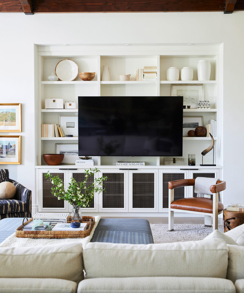 Neutral living room with tall decorated shelves, large black TV, cream sofa, artwork on walls, ottoman, leather lounge chair