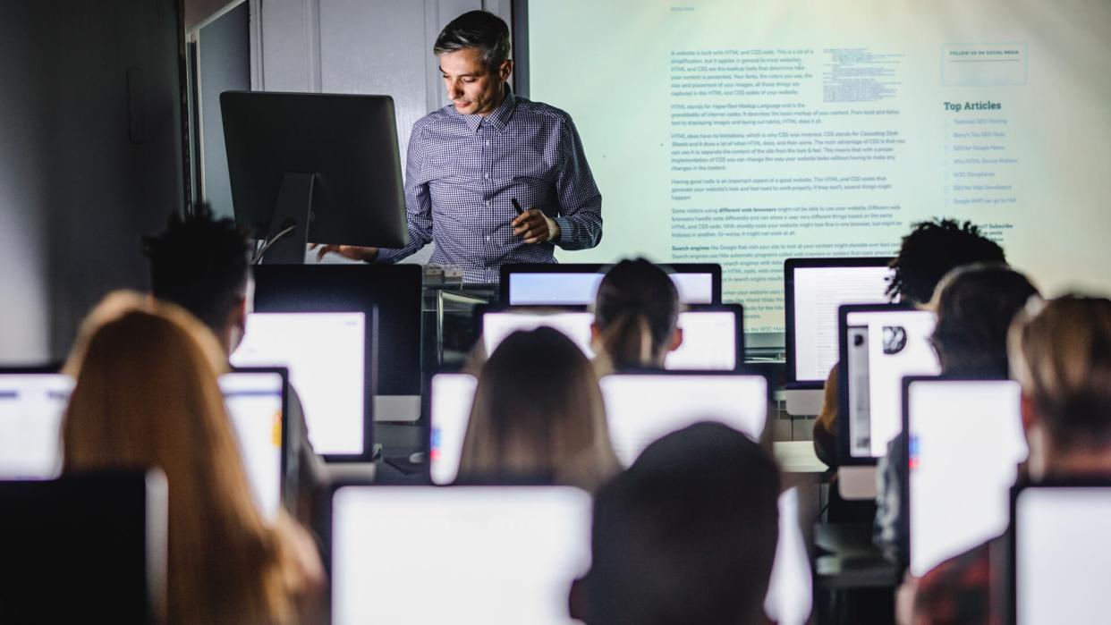 Male teacher giving a lecture from desktop PC during a class at computer lab.