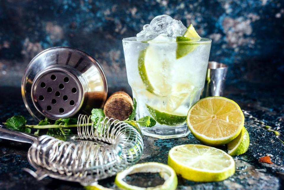 A gin drink surrounded by cocktail-making equipment and wedges of lime.