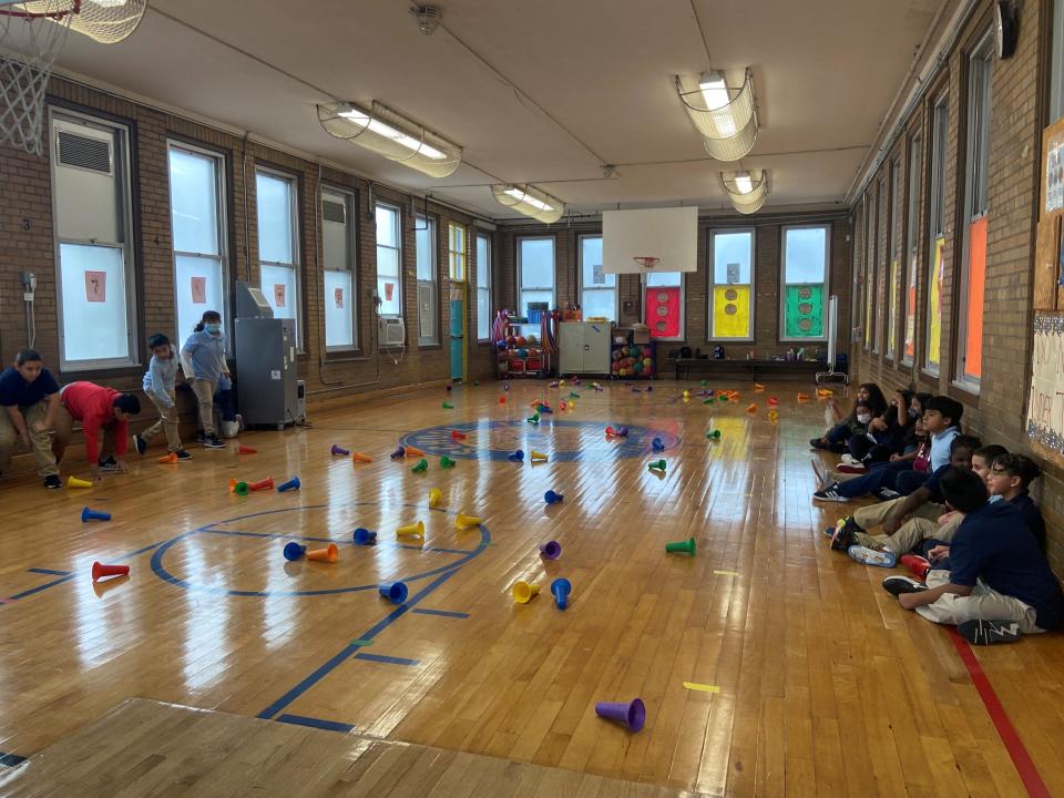 Students at School 19 in Paterson play "cleanies and messies" inside the gymnasium, racing to knock over and pick up multicolored cones.