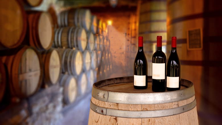 Red wine bottles beside oak aging barrels