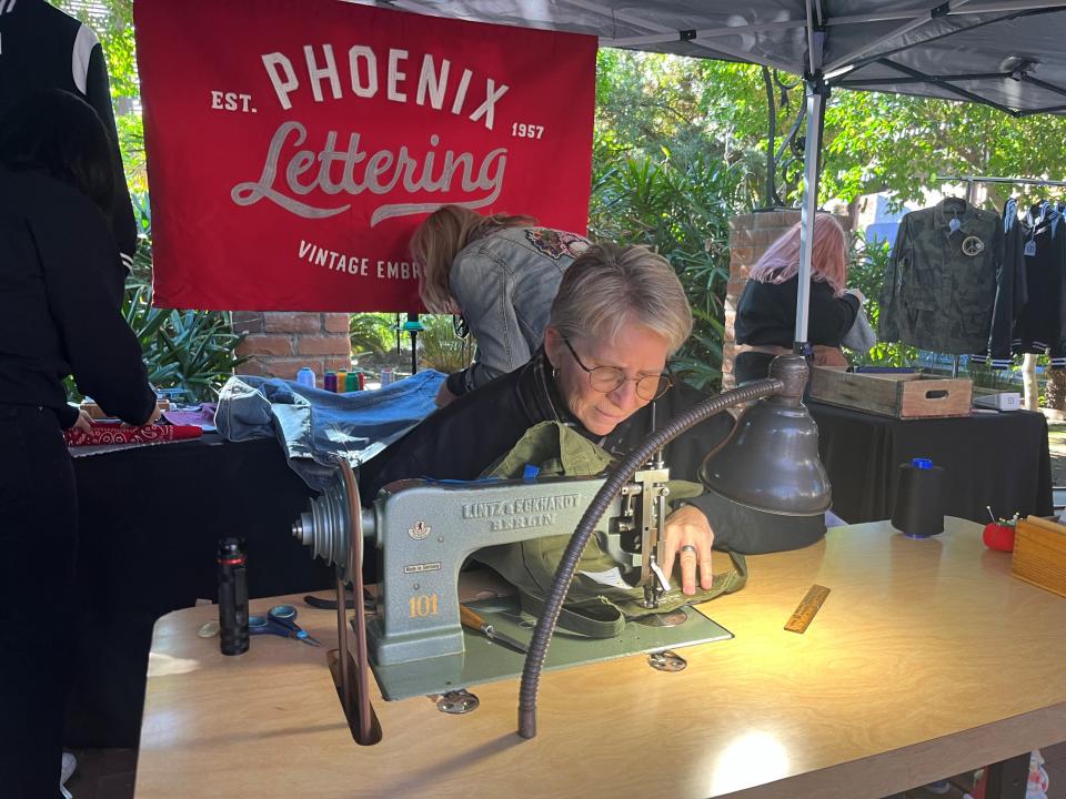 Sue Castelletti operates a chain stitching machine in the center of the Phoenix Lettering booth at the 2023 Phoenix Flea Market on Nov. 25, 2023.