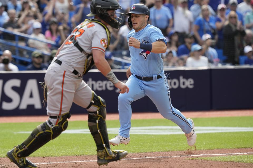 Toronto Blue Jays Daulton Varsho (25) scores the game-tying run as Baltimore Orioles catcher James McCann (27) waits for a throw during the tenth inning of a baseball game in Toronto, Sunday, May 21, 2023. (Frank Gunn/The Canadian Press via AP)