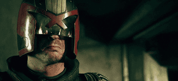 Judge Dredd wears helmet and fire reflects off the glass visor