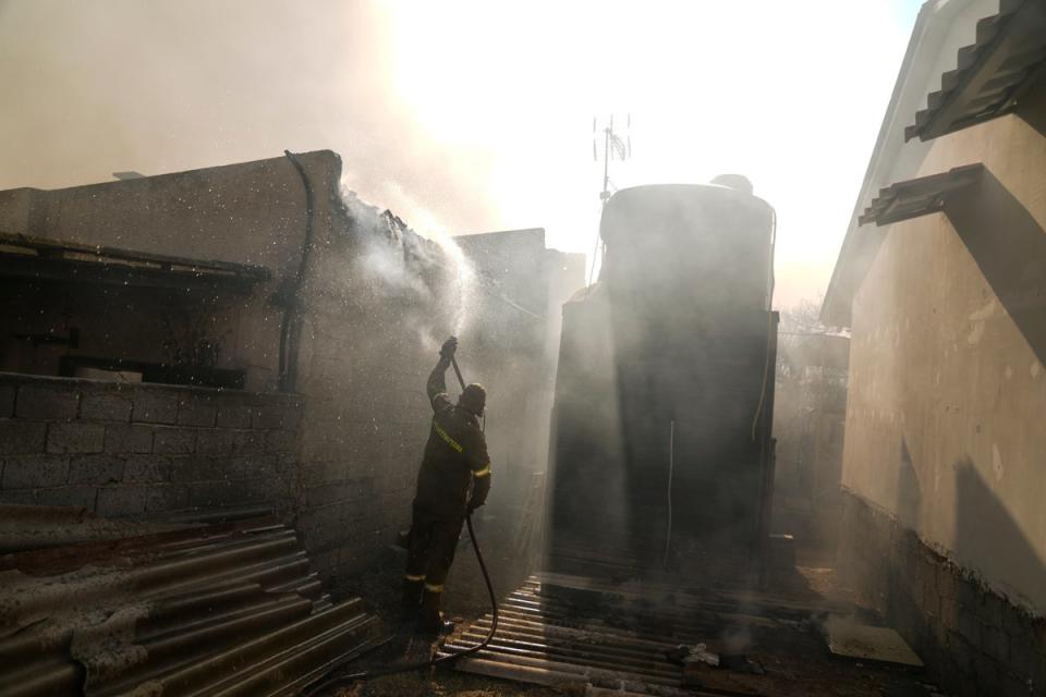 A firefighter aims water with a hose at a house near Loutraki 80 Kilometres west of Athens on Monday (AP)