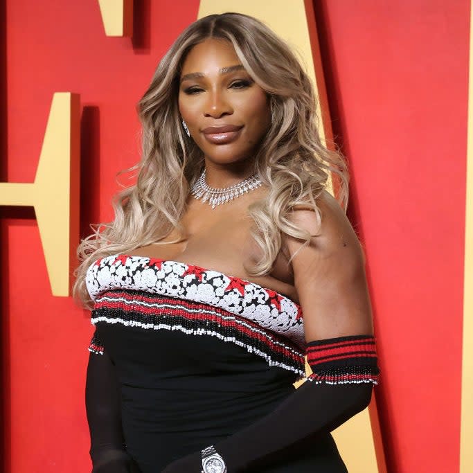 Serena Williams posing at an event in an elegant evening gown with a lace top and off-shoulder design