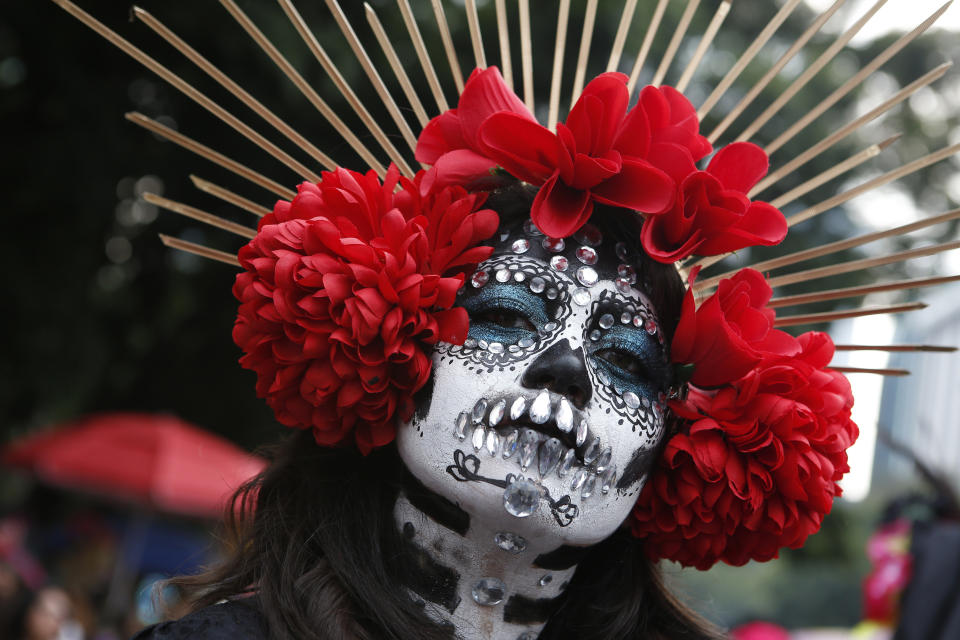 In this Oct. 26, 2019 photo, a woman dressed as a Catrina poses for a photo as she joins a parade on Mexico City's iconic Reforma Avenue during Day of the Dead celebrations. Mexico is marking its Day of the Dead amid the 500th anniversary of the Spanish Conquest, and true to the holiday’s roots, it has become a time for reflection and reconciliation, not revenge. (AP Photo/Ginnette Riquelme)