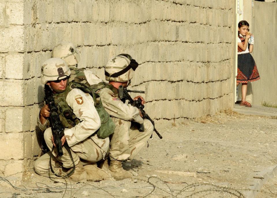 An Iraqi girl watches U.S. Army troops take cover in Mosul, Iraq, in 2003. <a href="https://media.gettyimages.com/id/2187982/photo/saddam-husseins-sons-confirmed-dead-in-u-s-raid.jpg?s=1024x1024&w=gi&k=20&c=j4ro-cgb1LUaxhO5tJRybqAMTPW9xfVY_OPX58TsGRg=" rel="nofollow noopener" target="_blank" data-ylk="slk:Scott Nelson/Getty Images;elm:context_link;itc:0;sec:content-canvas" class="link ">Scott Nelson/Getty Images</a>