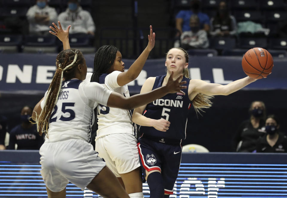 Connecticut guard Paige Bueckers (5) passes to a teammate against Xavier guards Carrie Gross (25) and Mackayla Scarlett, center, during the second half of an NCAA college basketball game Saturday, Feb. 20, 2021, in Cincinnati. UConn won 83-32. (AP Photo/Gary Landers)