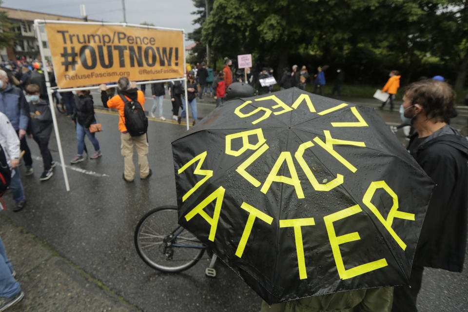 A person holds an umbrella that reads "Black Lives Matter" near a sign opposing Present Donald Trump and Vice President Mike Pence following a "Silent March" against racial inequality and police brutality that was organized by Black Lives Matter Seattle-King County, Friday, June 12, 2020, in Seattle. People marched for nearly two miles to support Black lives, oppose racism and to call for police reforms among other issues. (AP Photo/Ted S. Warren)