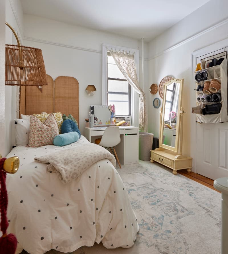 White bedroom with twin bed, natural room divider, rattan lamp, yellow floor mirror, vanity, and area rug.