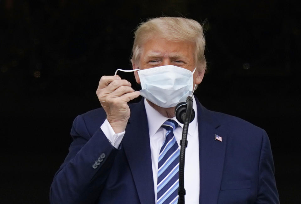 With two bandages on his hand, President Donald Trump removes his face mask to speak from the Blue Room Balcony of the White House to a crowd of supporters, Saturday, Oct. 10, 2020, in Washington. (AP Photo/Alex Brandon)