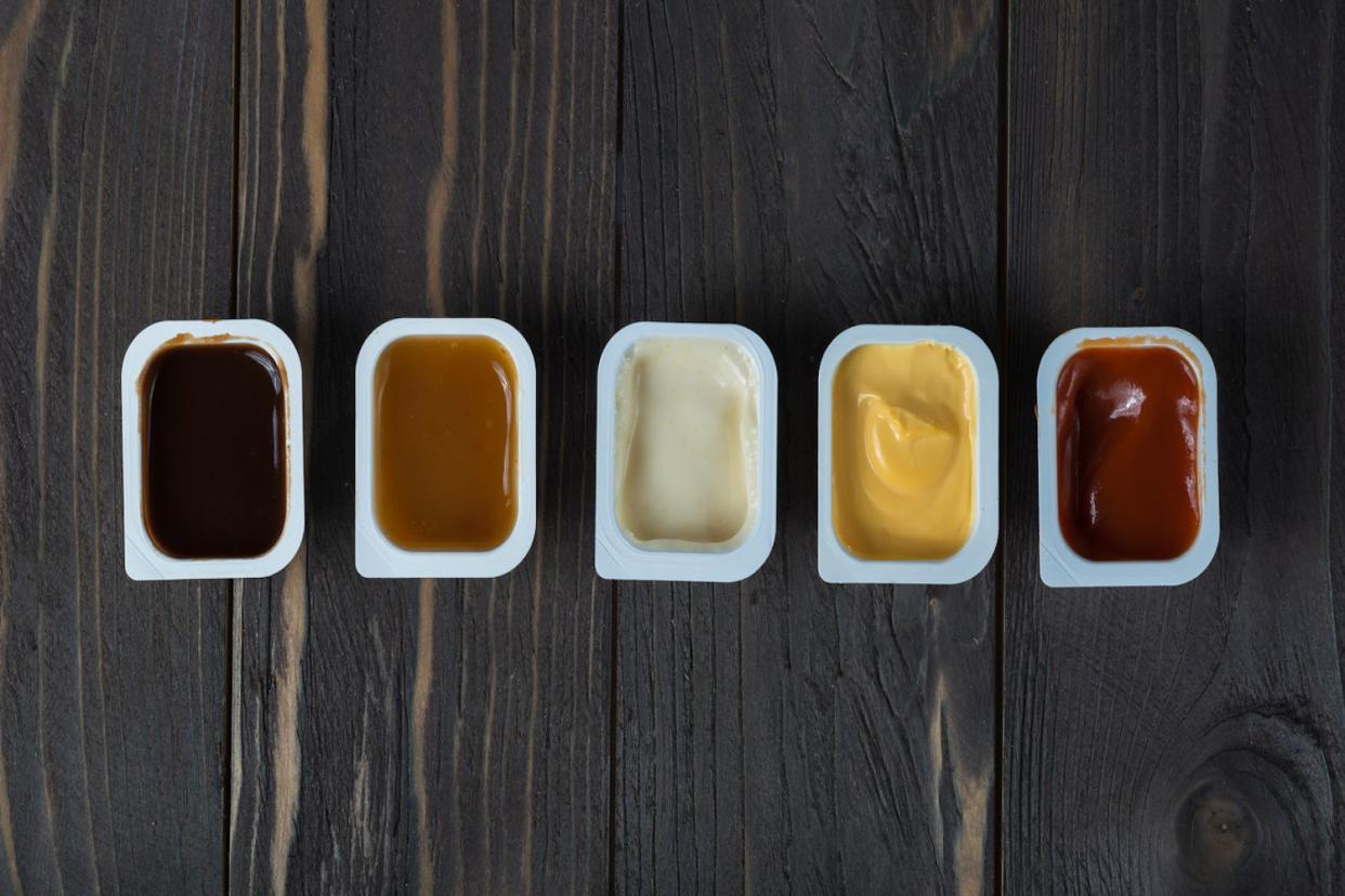 Five dipping sauces in plastic containers on dark wood table