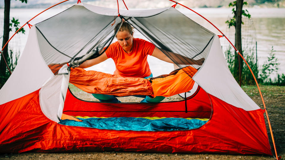 A woman lays out a sleeping bag inside a tent at a campground
