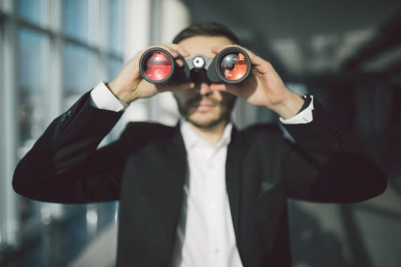 Person in business suit looking through binoculars