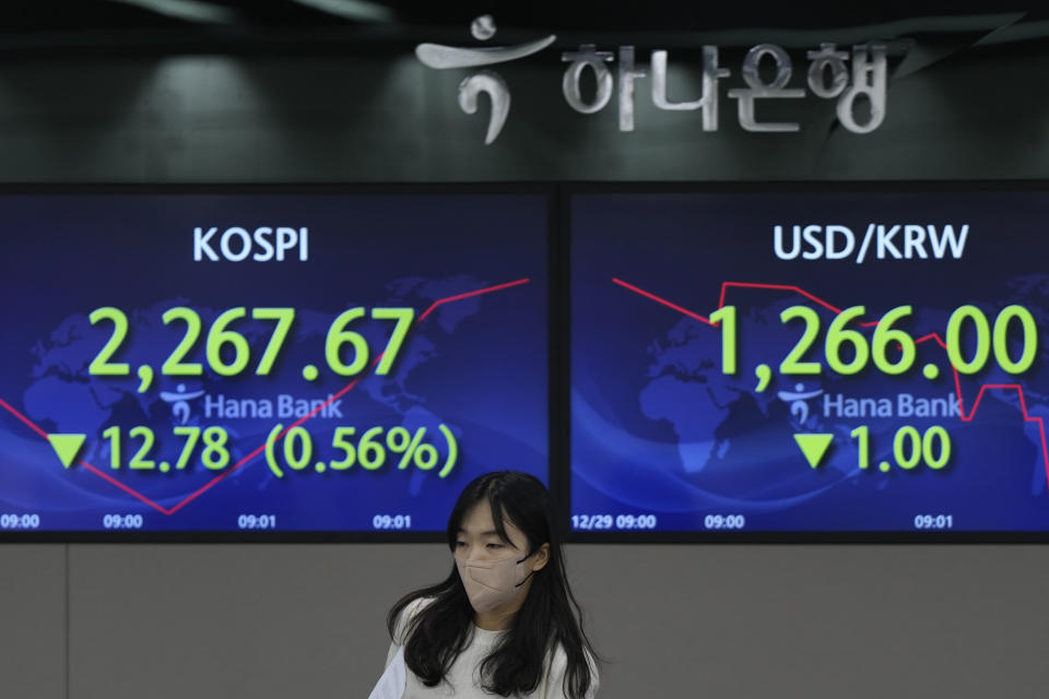 A currency trader walks by the screens showing the Korea Composite Stock Price Index (KOSPI), left, and the foreign exchange rate between U.S. dollar and South Korean won at a foreign exchange dealing room in Seoul, South Korea, Thursday, Dec. 29, 2022. Shares slipped in Asia on Thursday after benchmarks fell more than 1% on Wall Street in the middle of a mostly quiet and holiday-shortened week. (AP Photo/Lee Jin-man)