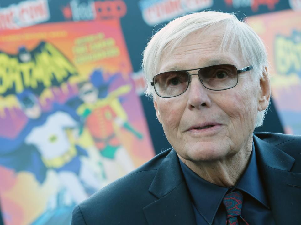 adam west in front of a vintage batman poster, wearing gradient sunglasses and a suit