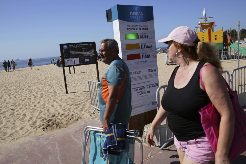 People arriving at the beach walk past a semaphore system that signals how crowded the beach is at any moment, in Oeiras, outside Lisbon, Wednesday, July 15, 2020. The system uses radar to count people entering the gates to the fenced beach to help beachgoers keep social distancing due to the coronavirus pandemic. (AP Photo/Armando Franca)