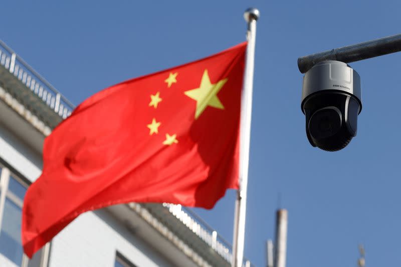 FILE PHOTO: A security surveillance camera overlooking a street is pictured next to a nearby fluttering flag of China in Beijing