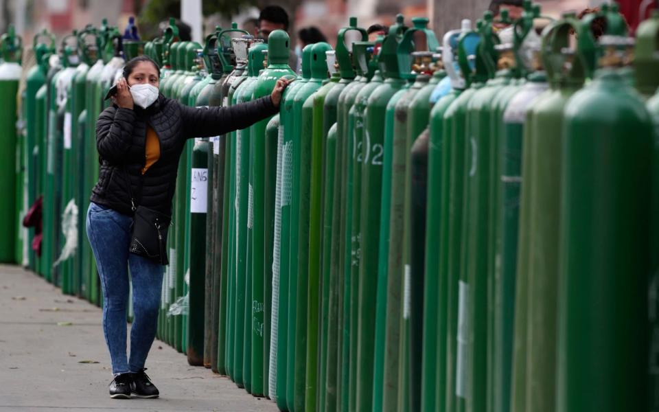 A woman stands next to an empty oxygen tank as she waits for a refill shop to open. - AP Photo/Martin Mejia