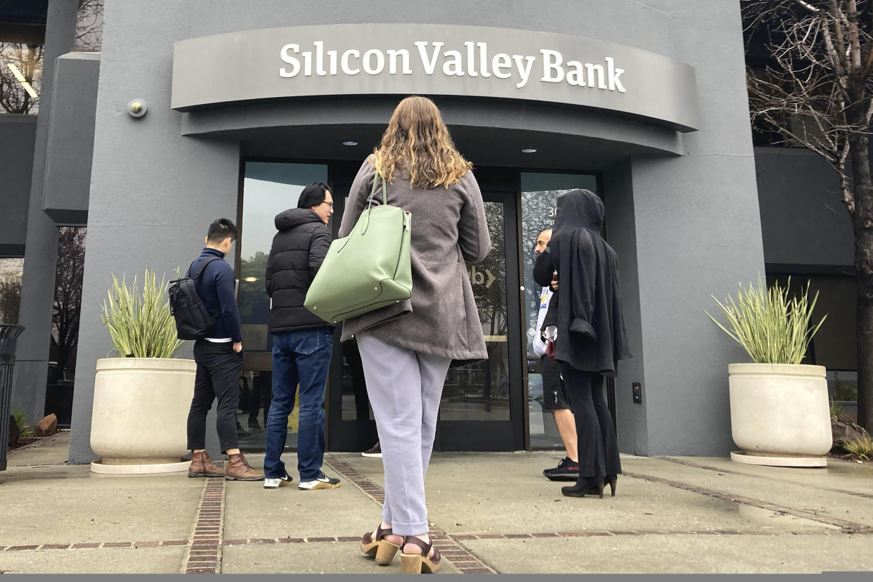 FILE - People stand outside a Silicon Valley Bank branch in Santa Clara, Calif., on March 10, 2023. The recent collapse of a trio of midsize banks, including Silicon Valley Bank, has once again raised questions on whether executive compensation is tilted toward short-term gains rather than companies' long-term health. (AP Photo/Jeff Chiu, File)