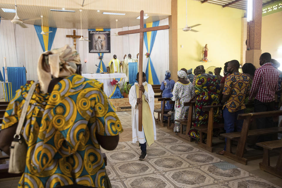 An altar boy carries a cross as Noel Henri Zongo, priest at the Church of the Sangoulé Lamizana military camp in Ouagadougou, Burkina Faso, celebrates Mass on Sunday, April 11, 2021. Just seven chaplains, hailing from Protestant, Catholic and Muslim faiths, are charged with spiritually advising some 11,000 soldiers and helping maintain their morale. (AP Photo/Sophie Garcia)