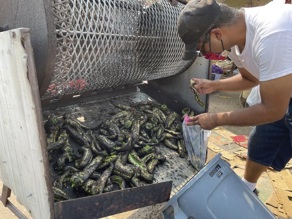 FILE - This July 12, 2021 image shows Israel Garcia bagging a batch of roasted green chile at a roadside stand in Hatch, N.M. There's nothing like the sweet smell of green chile roasting on an open flame. It permeates New Mexico every fall, wafting from roadside stands and grocery store parking lots, inducing immediate salivation and visions of mouth-watering culinary wonders laden with hot peppers. Democratic Sen. Bill Soules is proposing that roasted green chile become the official state aroma. (AP Photo/Susan Montoya Bryan, File)