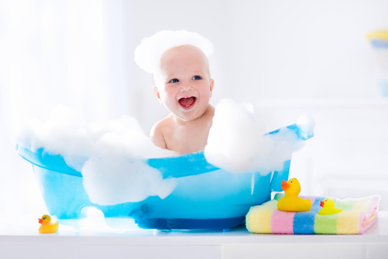 Happy laughing baby taking a bath playing with foam bubbles. Little child in a bathtub. Smiling kid in bathroom with colorful toy duck. Infant washing and bathing. Hygiene and care for young children.