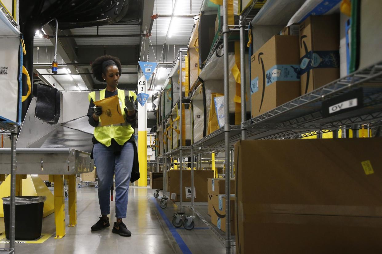 In this Dec. 17, 2019, photo Tahsha Sydnor stows packages into special containers after Amazon robots deliver separated packages by zip code at an Amazon warehouse facility in Goodyear, Ariz.