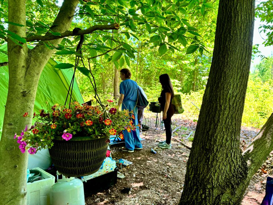 Outreach workers stand outside a man's tent in a Dover homeless encampment.