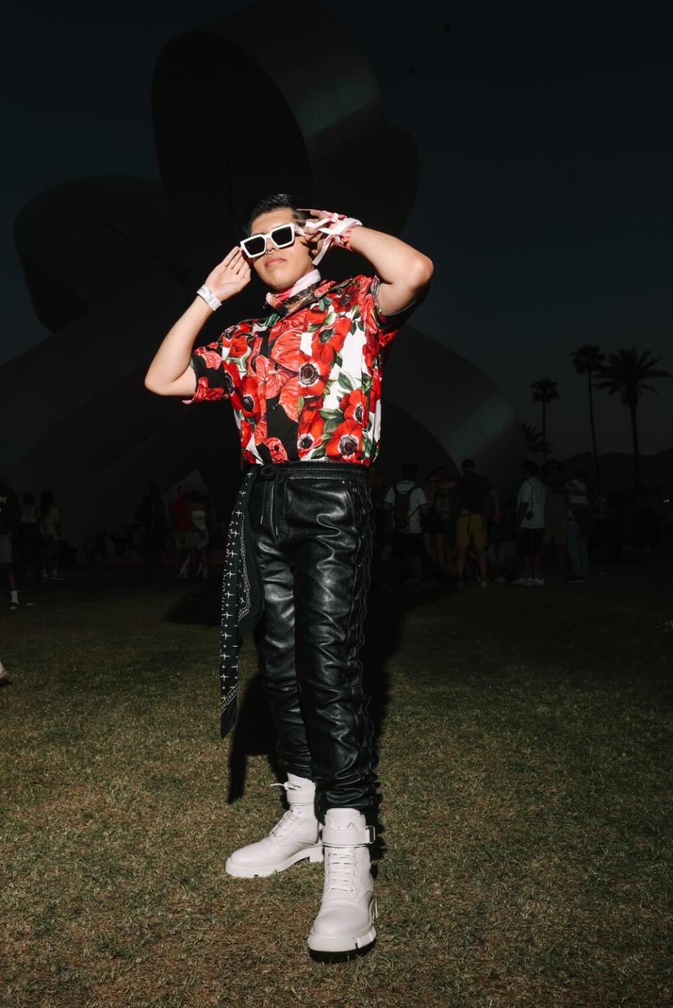 A man wearing a flower shirt and sunglasses poses with his hands behind his head