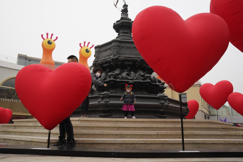 A visitor wearing a mask to protect from the coronavirus stand near heart shaped balloons displayed at a mall district during the second day of the Chinese Lunar New Year in Beijing on Saturday, Feb. 13, 2021. (AP Photo/Ng Han Guan)