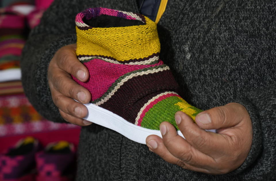 Lidio Herbas sostiene un zapato hecho con tejido andino en su taller de artesanía en El Alto, Bolivia, el jueves 23 de junio de 2022. Herbas ha usado un colorido y cálido tejido indígena quechua y aymara para hacer zapatos con diseños juveniles para mitigar el frío invernal. (Foto AP/Juan Karita)